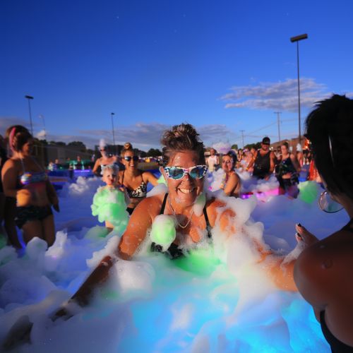 Woman enjoying a glow-in-the-dark foam party with colorful bubbles and vibrant lighting.