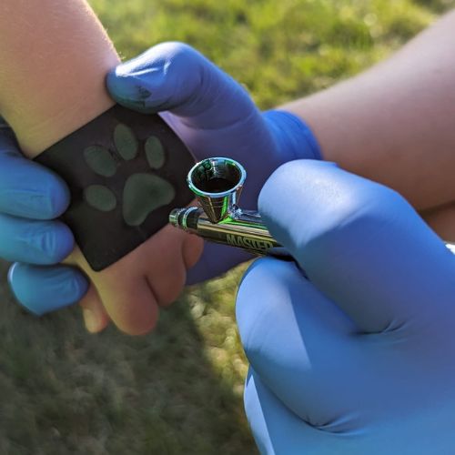 a childs small hand getting an airbrush tattoo of a cat paw on her hand.